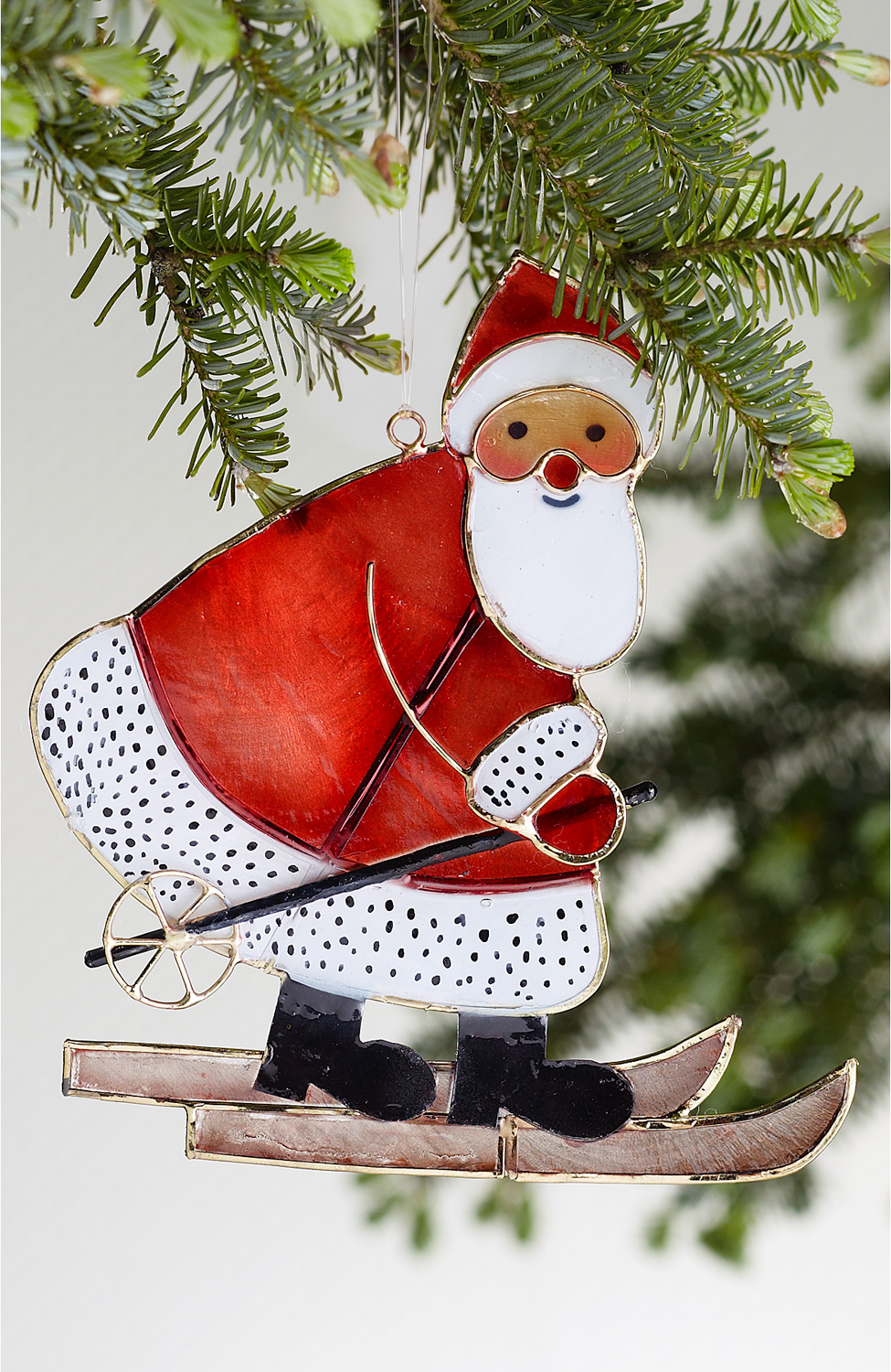 große rote Weihnachtsmann-Figur auf Skiern aus Metall, hängend an Tannenzweig, weißer Bart und rote Nase, schwarze Stiefel, klassische Weihnachtsdeko