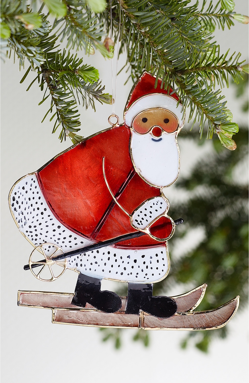 große rote Weihnachtsmann-Figur auf Skiern aus Metall, hängend an Tannenzweig, weißer Bart und rote Nase, schwarze Stiefel, klassische Weihnachtsdeko