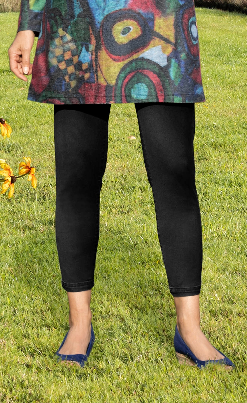 Schwarze Baumwoll-Mix-Hose, knöchellang, getragen zu buntem Oberteil und blauen Ballerinas, stehende Person auf Graswiese, linke Hand sichtbar
