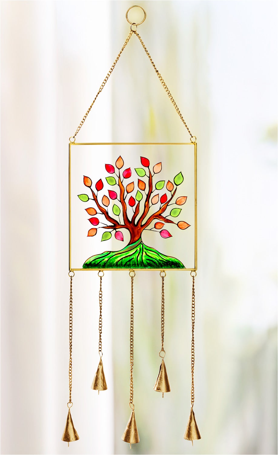 Fensterbild mit farbigem Baum-Motiv in Rot, Orange und Grün, Rahmen und Ketten in Gold, fünf Glocken hängen an goldenen Ketten unten, helles unscharfes Hintergrundlicht