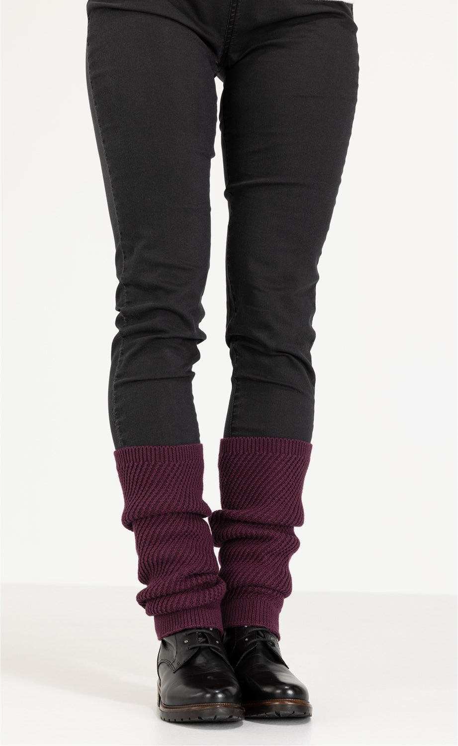 Beine in schwarzer Hose, schwarze Schnürschuhe, dunkelrote gestrickte Baumwoll-Mix-Stulpen, die lässig über den Schuhen getragen werden
