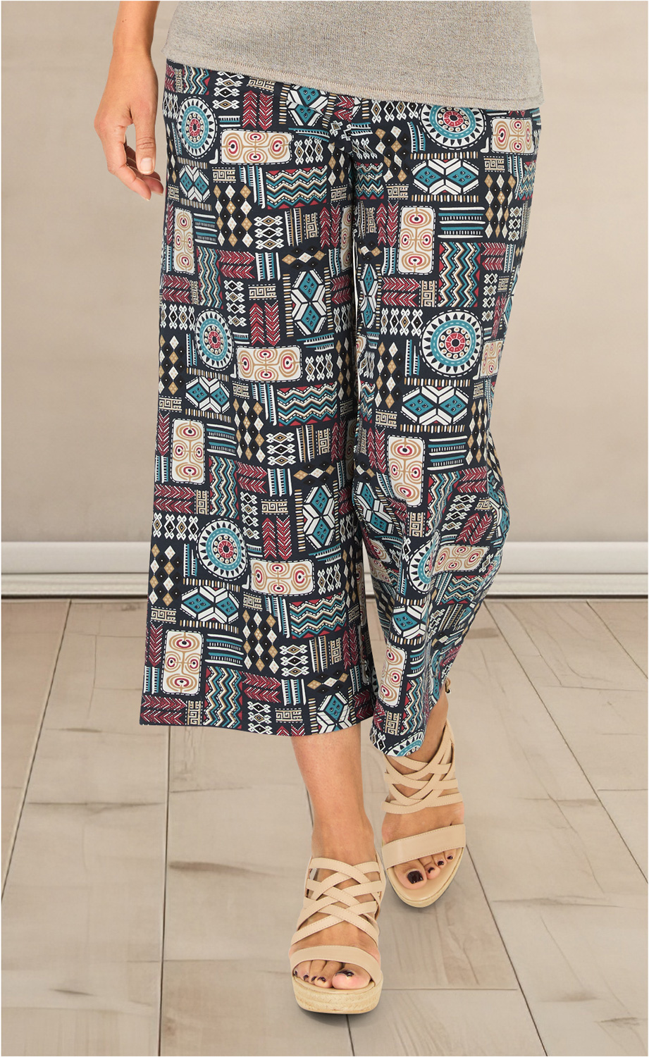 Baumwoll-Hose mit bunter Ethno-Musterung in Blau, Rot, Beige und Schwarz, weit geschnitten bis zur Wade, getragen mit beigefarbenen Sandaletten mit gekreuzten Riemen auf hellem Holzboden