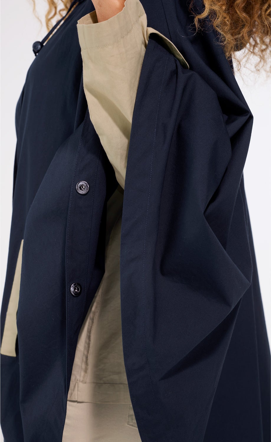 Detailaufnahme einer dunkelblauen Baumwoll-Jacke mit Knöpfen, getragen von einer Person mit beige-farbener Kleidung darunter, teilweise sichtbar, konzentriert auf den Ärmel und die Knopfleiste