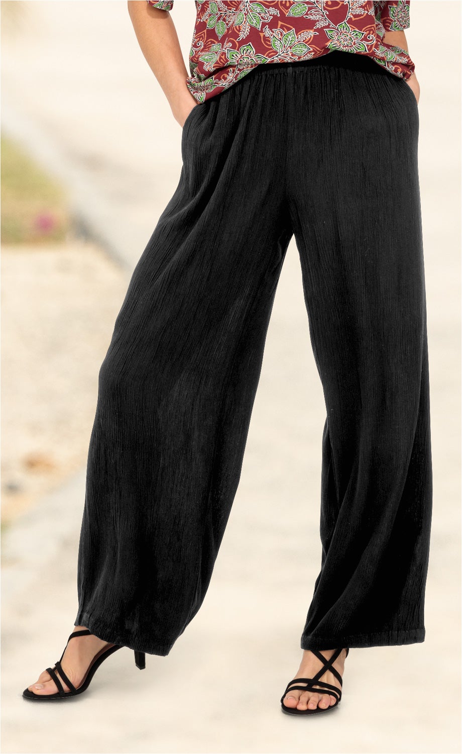 Schwarze, weite Viskose-Hose mit elastischem Bund, getragen von einer Person mit offenem, floralen Oberteil und schwarzen, hohen Sandalen mit dünnen Riemen.