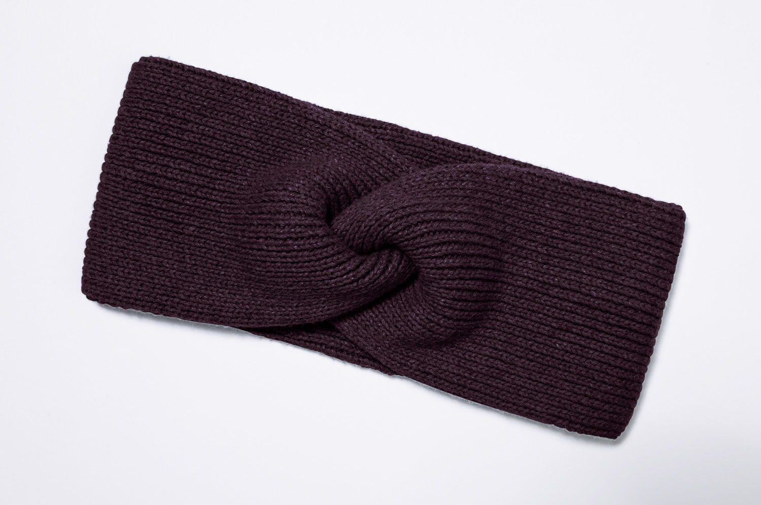 dunkelviolettes, gestricktes Baumwoll-Mix-Stirnband mit gedrehtem Knoten-Motiv, liegend auf weißem Hintergrund