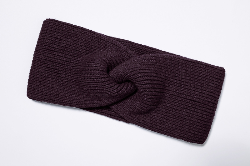 dunkelviolettes, gestricktes Baumwoll-Mix-Stirnband mit gedrehtem Knoten-Motiv, liegend auf weißem Hintergrund