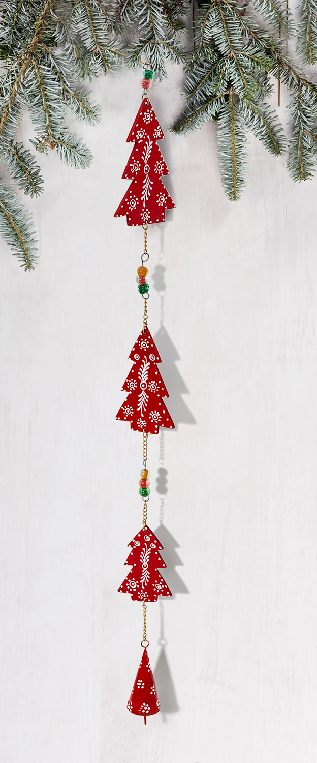Rote Girlande mit weißen floralen Mustern, bestehend aus drei stilisierten Tannenbäumen und einem kleinen rot dekorierten Glockenanhänger, verbunden durch goldene Ketten und bunte Perlen, aufgehängt an verschneiten Tannenzweigen.