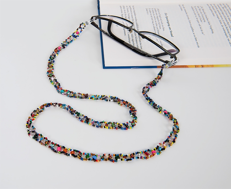 schwarze Brille mit bunter, aus kleinen Perlen gefertigter Brillenkette, Brille liegt auf aufgeschlagenem Buch mit Text, weiße Oberfläche
