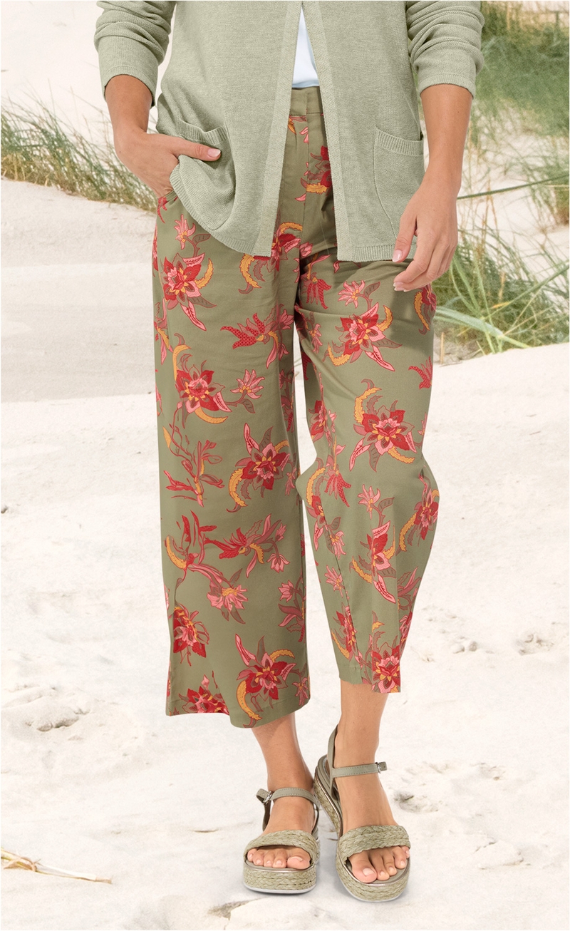 Baumwoll-Mix-Hose in khaki mit weitem Bein und floralem Muster in rot, pink und gelb, kombiniert mit grünem Strickcardigan, Pop-up-Sandalen mit geflochtenem Riemen, Strand und Dünen im Hintergrund