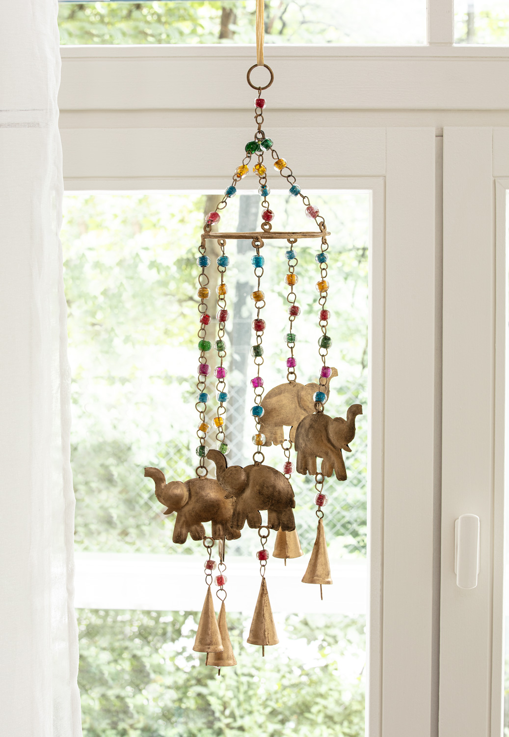 Metall-Mobile 60cm mit drei goldfarbenen Elefanten, bunten Glasperlen und kleinen Glocken, hängend vor einem Fenster mit weißem Vorhang und grünem Hintergrund draußen