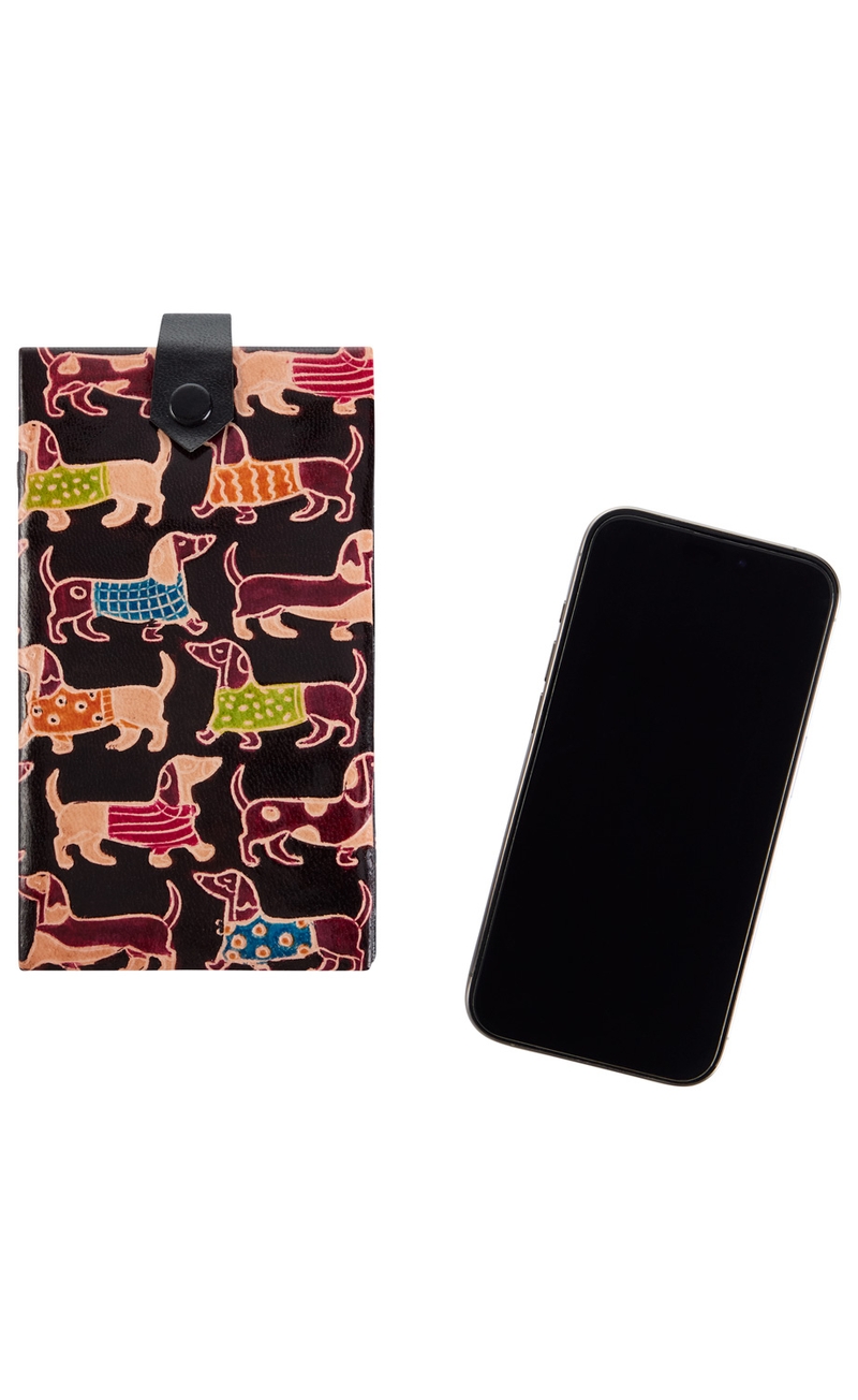 schwarze Handytasche aus Leder mit bunten Dackel-Motiven, daneben schwarzes Smartphone mit ausgeschaltetem Display auf weißem Hintergrund
