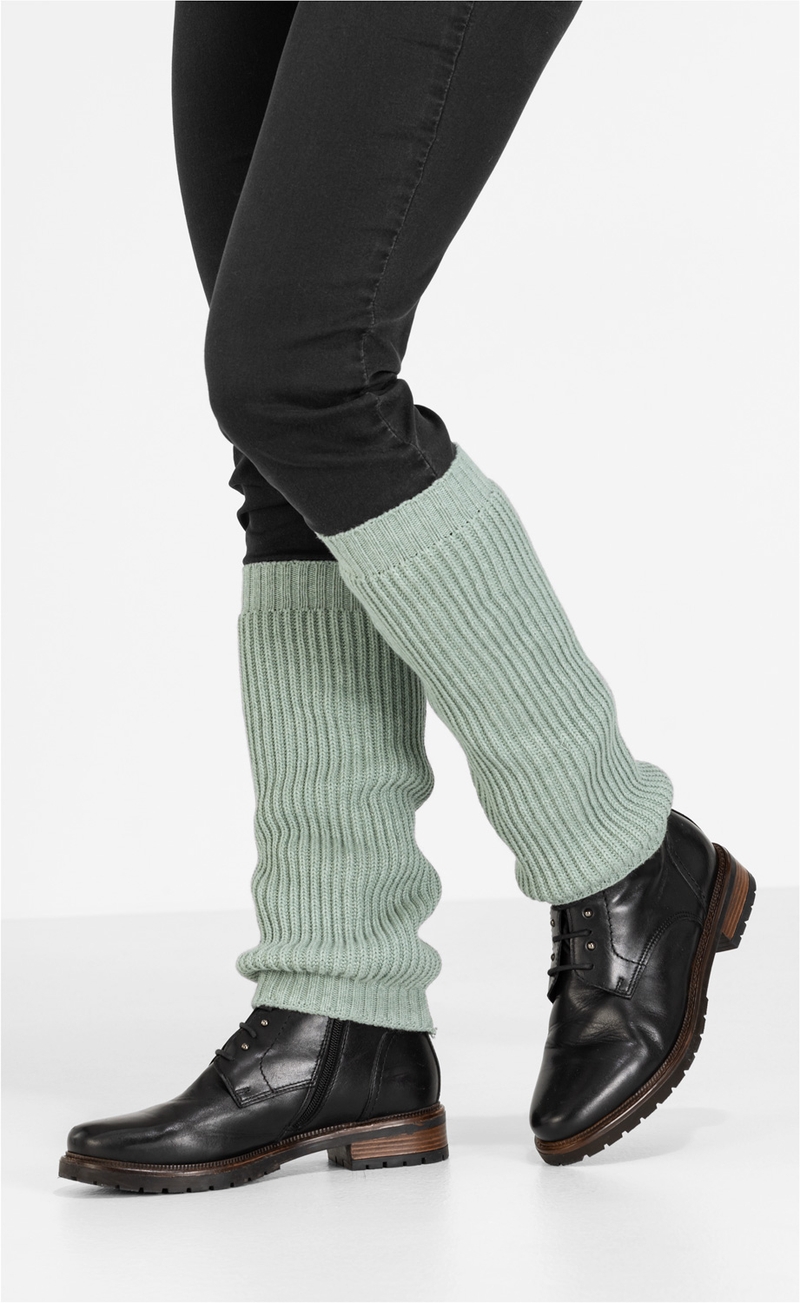 Beine mit schwarzen Hosen, hellgrüne grob gestrickte Baumwoll-Mix-Stulpen über den Waden, schwarze Lederstiefel mit Schnürung und Reißverschluss, weiße Hintergrundfläche