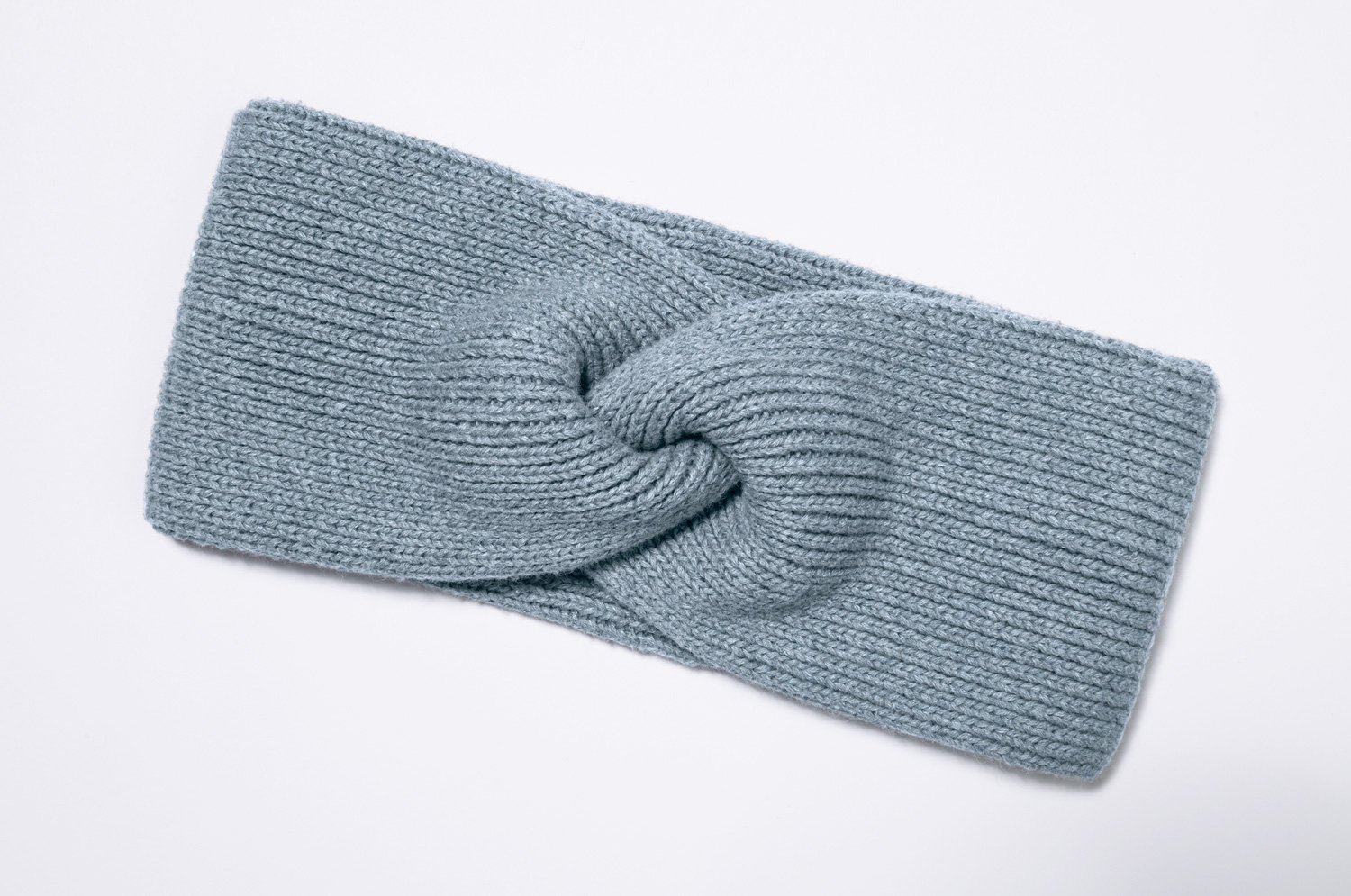 Hellblaues, gestricktes Baumwoll-Mix-Stirnband mit gedrehtem Knoten-Detail, flach liegend auf weißem Hintergrund, weiche und warme Struktur, für kühlen Wettergebrauch geeignet