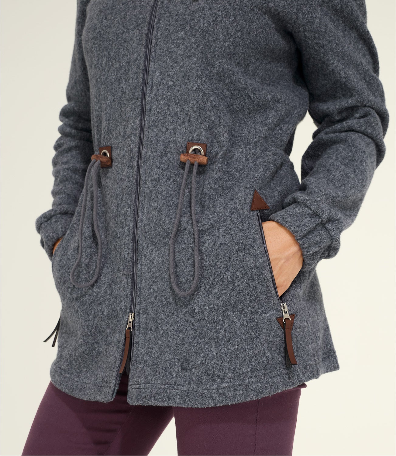 Graue Baumwoll-Jacke mit Reißverschluss, zwei Taschen mit Reißverschluss, verstellbaren Kordeln an der Taille und elastischen Bündchen an den Ärmeln, getragen von einer Person mit dunkler Hose