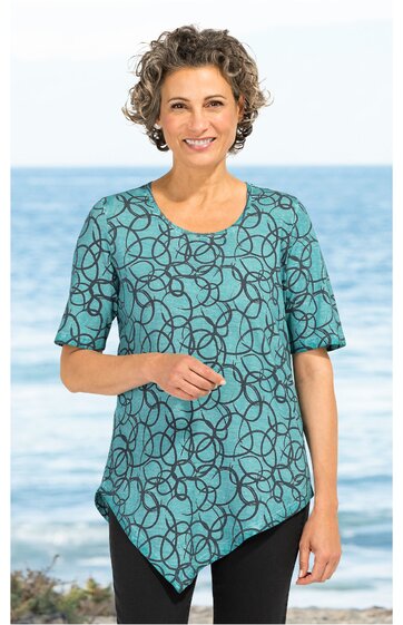 Türkisfarbenes, kurzärmeliges Damenoberteil mit schwarzem, unregelmäßigem Kettenmuster, rundem Halsausschnitt, asymmetrischem Saum, getragen von lächelnder Frau vor Meereskulisse
