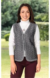 Graue Strickweste mit Strickmuster, V-Ausschnitt, ohne Verschluss, gerade geschnitten, getragen von stehendem weiblichen Modell mit weißem Rollkragenpullover und bordeauxroter Hose, Outdoor-Hintergrund