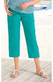 Türkise Caprihose, gerade geschnitten, hüfttief, ohne sichtbare Verschlüsse, getragen von stehender Person, kombiniert mit weißer Sandale und blau gemustertem Oberteil