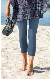 Dunkelblaue Capri-Leggings, enganliegend, knielang, getragen von stehendem Modell, barfuß, links handhaltend schwarze Schnürschuhe mit Ösen, darüber Teil eines blaugrauen Oberteils mit dunkelroten Spiralmustern