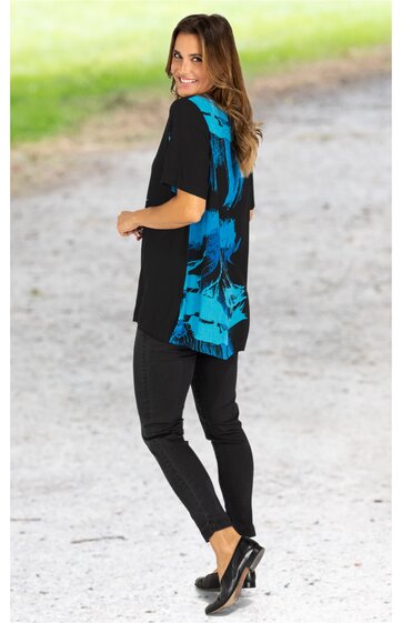 Schwarze Damenbluse mit blauem abstraktem Muster auf Rückseite, kurze Ärmel, leichter Rundhalsausschnitt, locker geschnitten, getragen von stehender Frau mit Blick über die Schulter, kombiniert mit schwarzer Hose und schwarzen Schuhen