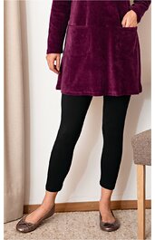 Schwarze Leggings, eng anliegend, knöchellang, getragen von stehender Person, kombiniert mit violettem, langem Oberteil mit großen Taschen und braunen Ballerinas