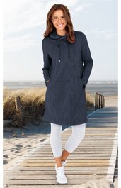 Dunkelblauer Kapuzenpullover als langes Kleid, ohne Muster, mit Kängurutasche vorne, lange Ärmel, Kapuze mit Kordeln, getragen von stehender Frau, kombiniert mit weißen Leggings und weißen Sportschuhen