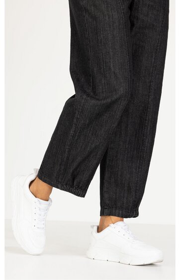 Weiße Sneaker mit dicker Sohle, runde Zehenpartie, Schnürung vorne, getragen von stehender Person in schwarzen, weit geschnittenen Jeans