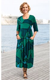 Maxikleid in dunklem grün mit dunkelblauem abstraktem Muster, Rundhalsausschnitt, dreiviertellange Ärmel, lockere A-Linie, seitliche Eingrifftaschen, getragen von lächelnder stehender Frau, kniehoch