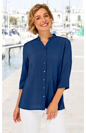 Damenbluse in Marineblau, unifarben, Stehkragen, durchgehende Knopfleiste, 3/4-Arm, gerade geschnitten, getragen von lächelnder, stehender Frau am Wasserhafen