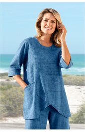 Blaues Zweiteiler-Outfit mit feinem Karomuster, langärmliges Oberteil mit Rundhalsausschnitt, asymmetrischer, spitz zulaufender Saum, seitliche Nahttaschen, weite gerade geschnittene Hose, getragen von stehender Frau am Strand