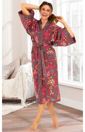 Roter Morgenmantel mit dichten Blumenmustern in Grün, Gelb und Blau, langer Ärmel, Bindegürtel in der Taille, stehende Frau mit erhobenem linken Arm und lachendem Gesicht, knielang