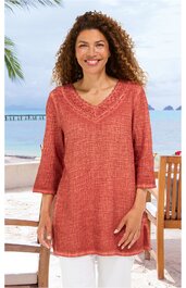 Lachsfarbenes langärmeliges Tunika-Oberteil mit V-Ausschnitt, Spitzenbesatz am Hals, lockere Passform, getragen von stehender Frau, halbtransparentes Strukturmuster