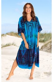 Locker geschnittenes Kaftankleid in Blau mit schwarzen geometrischen Mustern, V-Ausschnitt, halblange weite Ärmel, knielang, getragen von stehender lachender Frau am Strand