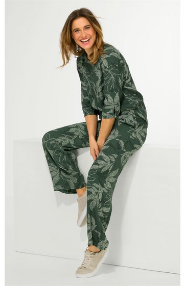 Damenjumpsuit in dunkelgrün mit hellgrünem Blumenmuster, lange Ärmel mit Bündchen, runder Ausschnitt, lockere Passform, getragen von sitzender Frau, bequeme Freizeithose mit weitem Bein
