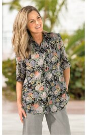 Langärmelige Bluse mit floralem Muster in Grün, Orange und Grau auf schwarzem Grund, Hemdblusenkragen, Knopfleiste, getragen von stehender lächelnder Frau, locker geschnitten