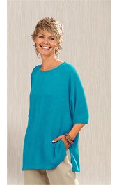 Türkisfarbener Pullover mit weitem U-Boot-Ausschnitt, halblangen Ärmeln, lockerer gerader Form, seitliche Taschen, getragen von stehender Frau mit kurzer blonder Frisur