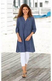 Blau kariertes, langärmeliges, knieumspielendes Kleid mit V-Ausschnitt, ohne sichtbare Knöpfe, lockere Passform, getragen von stehender Frau, kombiniert mit weißen Leggings und Sandalen