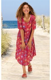 Rotes midikurzärmeliges Kleid mit rundem Ausschnitt, rundem mehrfarbigem Blumenmuster, knielang, tailliert, getragen von lächelnder stehender Frau, Sandalen