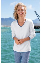 Weißer Pullover mit weitem V-Ausschnitt, graublauer Rand am Ausschnitt, lange Ärmel, getragen von lächelnder Frau vor Wasser und Bergen, lockere Passform