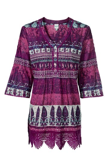 Tunika in dunkelviolett mit weißen und dunkelblauen floralen und geometrischen Mustern, V-Ausschnitt mit Knopfleiste, 3/4-Ärmel mit leichter Glockenform, seitliche Schlitze, unterer Saum mit Spitzenbesatz