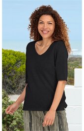 Schwarzes Kurzarmshirt mit V-Ausschnitt, gerade geschnitten, getragen von lächelnder Frau mit lockigen Haaren, im Stehen, Outdoor-Hintergrund mit Pflanzen und Himmel