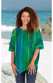 Locker sitzendes T-Shirt in Grün- und Blautönen mit vertikalen Streifen, Rundhalsausschnitt, kurze Ärmel, getragen von lächelnder Frau am Strand, gerade Pose