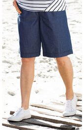 Dunkelblaue knielange Shorts ohne Muster, gerade geschnitten, getragen von stehender Person mit weißem gestreiftem Oberteil und weißen Sneakers auf Sandboden