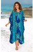 Kaftan in dunkelblau und türkis mit großflächigem floralem Muster in grün und hellblau, V-Ausschnitt, weite Form, knöchellang, getragen von lächelnder stehender Frau am Strand