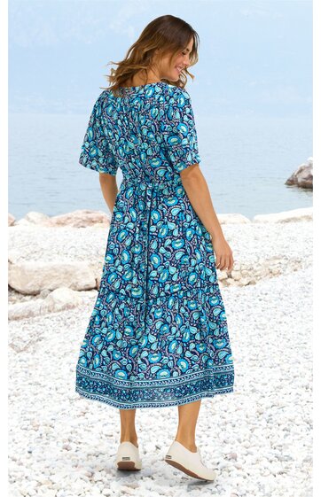 Midikleid in Blau mit türkis-rosa geometrischem Muster, halblange Ärmel, rundhals, tailliert mit Bindegürtel, weite Rockpartie, getragen von rückwärts blickender stehender Frau am Strand