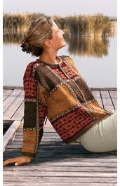 Langärmliges Pullover mit rundem Ausschnitt, gemustert in Rot-, Braun- und Gelbtönen, geometrisches Design mit unterschiedlich großen Rechtecken und Rautenmuster, getragen von seitlich sitzender Frau am Steg vor Wasser und Schilf