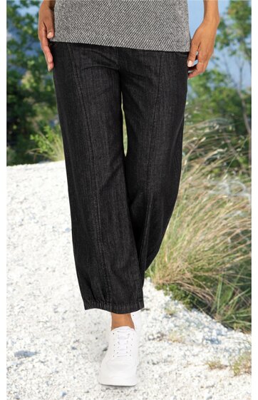 Schwarze Hose mit weitem Bein, glatter Oberfläche, elastischer Bund, getragen von stehender Person, kombiniert mit weißer Sportjacke und weißen Sportschuhen