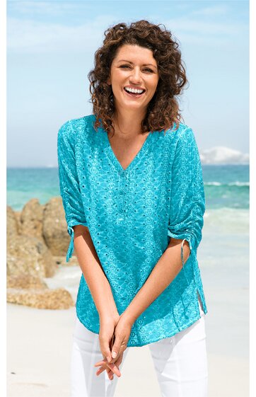 Türkisblaues Damenblusenshirt mit floralem Muster, V-Ausschnitt, 3/4-Ärmel mit Tunnelzug, leicht tailliert, getragen von stehender lachender Frau vor Strandkulisse