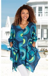 Longbluse in Blautönen mit ungewöhnlichem Kreismuster in Hellblau, Türkis und Grün, asymmetrischer Saum, V-Ausschnitt, 3-4-Arm, zwei große seitliche Taschen, getragen von lächelnder Frau im Freien