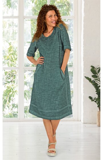 Grünes, knielanges Kleid mit Taschen, Rundhalsausschnitt, halblangen Ärmeln, locker geschnitten, getragen von stehender Frau mit verschränkten Armen, leichte Struktur im Stoff