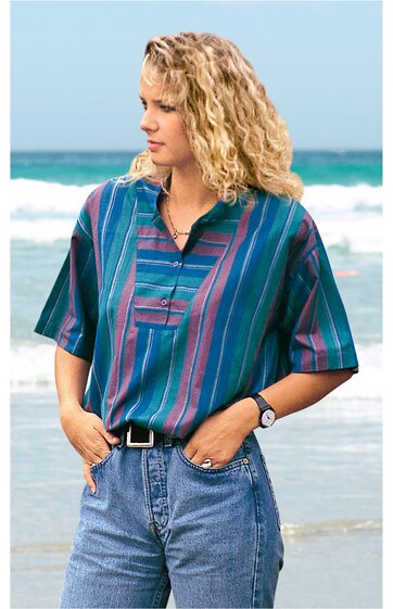 Kurzärmliges Hemd in Blau mit senkrechten Streifen in Dunkelrot und Violett, V-Ausschnitt mit kurzer Knopfleiste, getragen von stehender Frau mit blonden lockigen Haaren, kombiniert mit blauer Jeans und schwarzem Gürtel